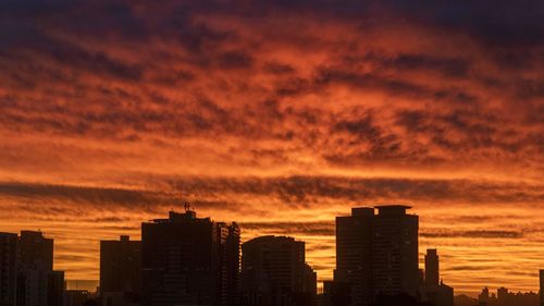 Silhouette buildings against dramatic sky during sunset