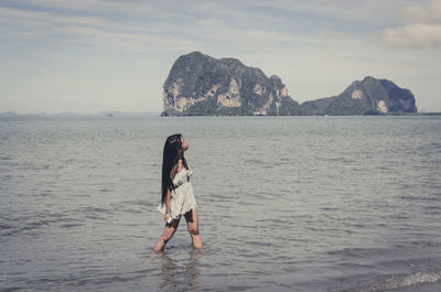 Young woman looking up while standing in sea against sky