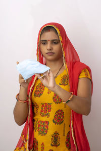 Portrait of woman holding flu mask standing against white background