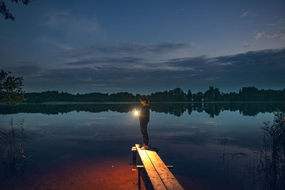 A girl with a flashlight stands on the shore of the lake, illuminates the way to the shore