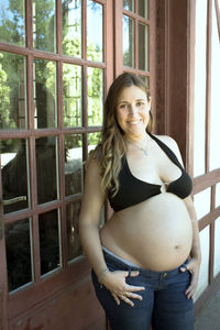 Portrait of smiling pregnant woman standing against window