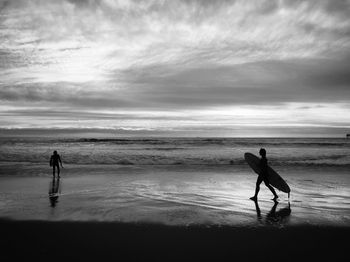 Silhouette people walking on beach against sky