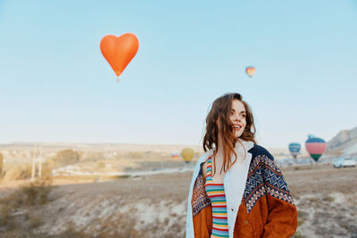 Rear view of young woman with balloons against sky