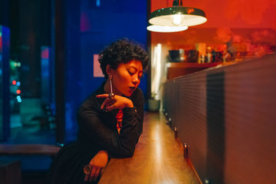 Woman looking away while sitting in illuminated building