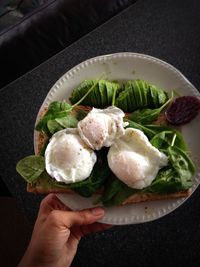 Cropped hand of person holding plate of poached eggs and bread on table