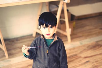 Portrait of boy holding paintbrush on hardwood floor