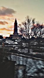 Bare trees against buildings at sunset