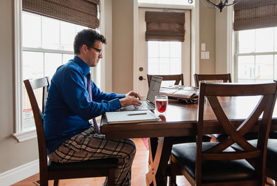 Man on cellphone working from home using a computer in pyjama pants.