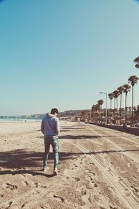 Rear view of man standing on beach against clear sky