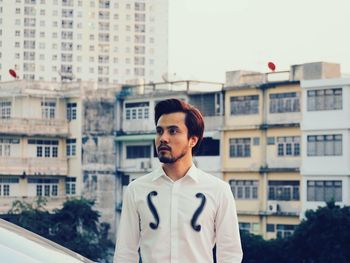 Portrait of young man standing against buildings in city