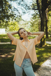 Portrait of young woman standing by tree at park