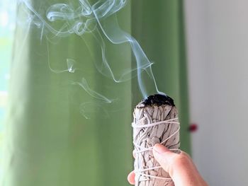 Close-up of hand holding smoking bundle of white sage 