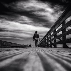 Rear view of man walking on road against cloudy sky