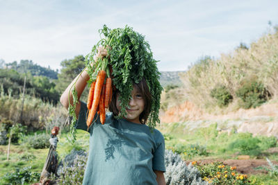 Boy standing in vegetable garden, holding a bunch of carrots