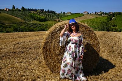 Portrait of smiling mid adult woman standing by hay bale on field