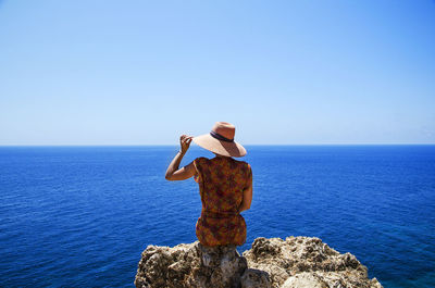 Rear view of woman sitting on rock against sea and sky