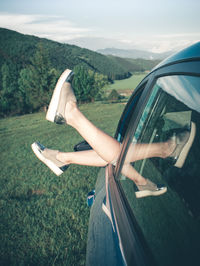 Close-up of legs by car on road against sky