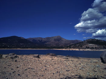 Scenic view of land and mountains against blue sky and a lake