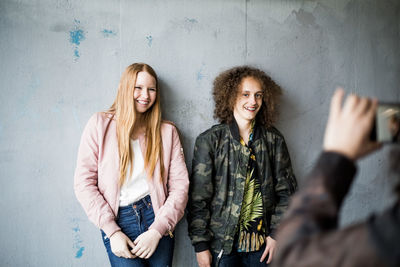 Cropped image of teenage girl photographing friends standing against wall at parking garage