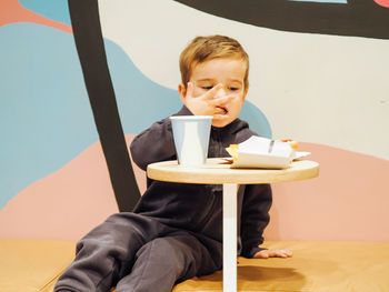 Cute toddler boy in casual clothes eating in a food court