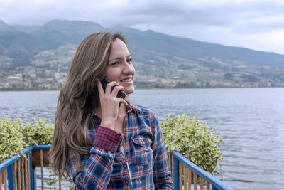 Young woman using smart phone by lake against mountains