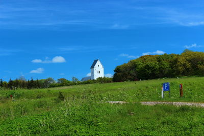 House on grassy field against cloudy sky