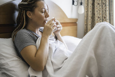 Woman sits in bed and drinks water.