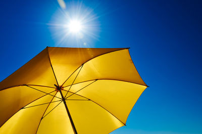 Low angle view of yellow umbrella against blue sky