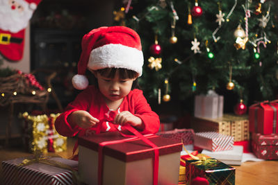 Cute girl opening christmas present against tree at home
