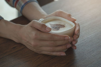 High angle view of woman holding coffee cup on table