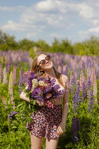 Young caucasian beautiful woman in the flowers field holding a bunch of lupins