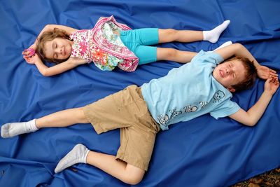 Directly above shot of siblings relaxing on blue fabric at field