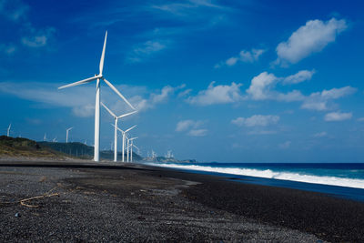 Wind turbines on beach against blue sky