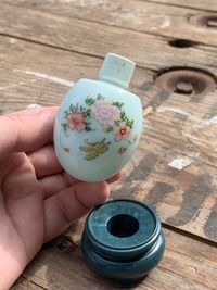 High angle view of hand holding a blue floral vintage perfume bottle on table