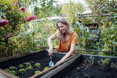 Smiling blond woman with shovel gardening in backyard