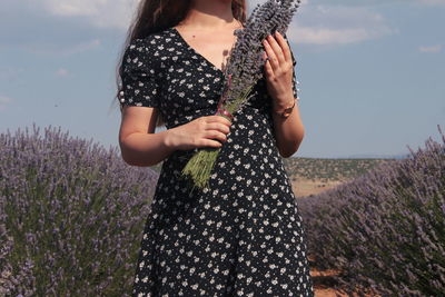 Midsection of woman standing with lavenders on field