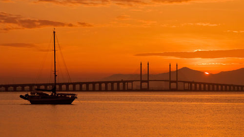 Silhouette of suspension bridge against cloudy sky during sunset