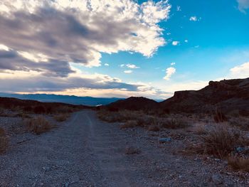 Dirt road leading towards mountains against sky