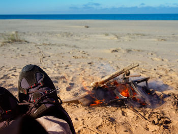 Low section of person sitting by campfire at beach