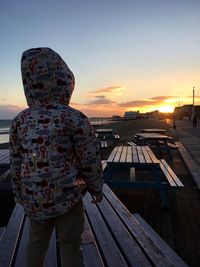 Rear view of man standing on picnic table against sky during sunset