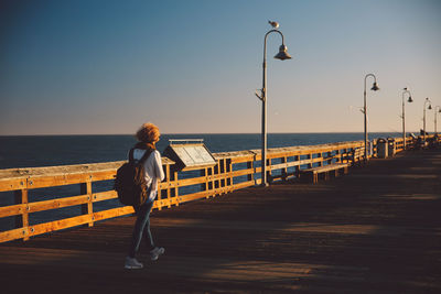 Full length of mid adult woman walking on pier over sea during sunset