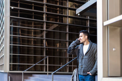 Man using smartphone outdoors, standing next to office building