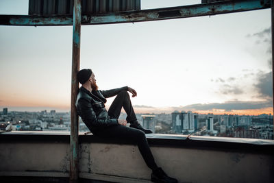Side view of man sitting on railing against cityscape