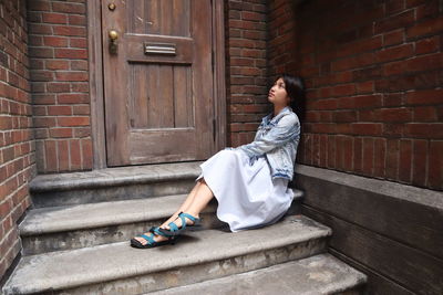 Full length of young woman sitting by closed door