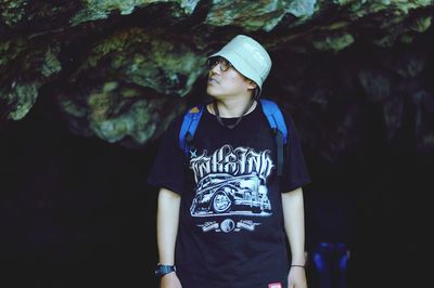 Young man looking away while standing against trees