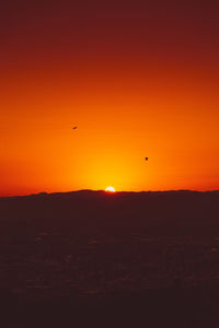 Silhouette of birds flying against orange sky