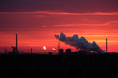 Silhouette factory against orange sky