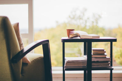 Books on table by armchair against window at home