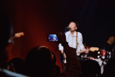 Rear view of woman photographing singer through mobile phone at music concert
