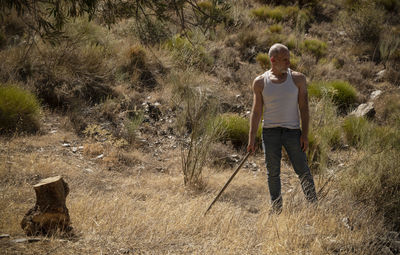 Adult man in white tank top and jeans working on field in summer